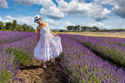 Beautiful woman posing in a blooming lavender field with her white dress and hat. 