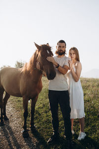 Couple standing by horse on land against sky