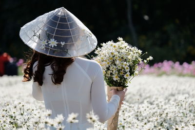 A girl with hat and flowers in flowers field. costume tradition of vietnam. view from behind 