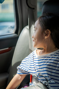 Young little girl enjoying the trip in back seat looking out the window of the car