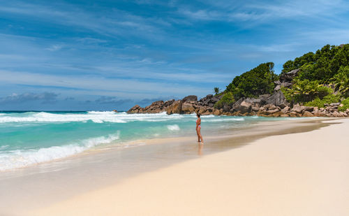 Woman standing alone on tropical sandy beach with idyllic turquoise ocean and waves