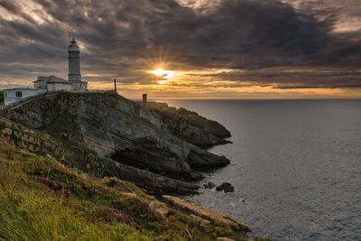 Lighthouse by sea against sky during sunset