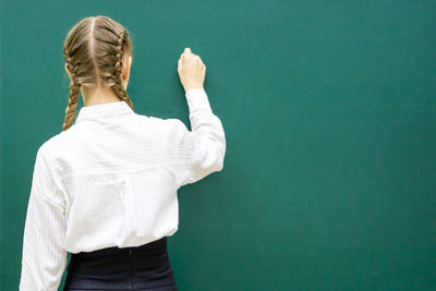 Rear view of girl writing on blackboard