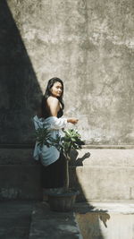 Woman standing by potted plant against wall