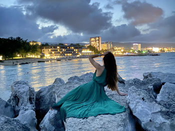 Woman standing on rock by sea against sky