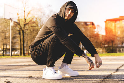 Portrait of young man crouching on land in city