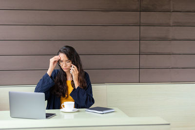 Young woman using mobile phone while sitting on table