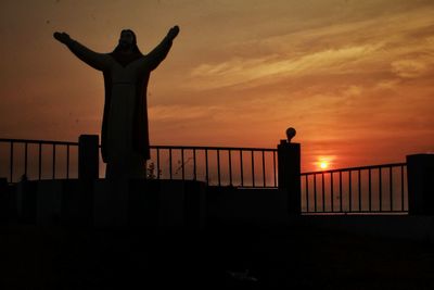 Silhouette man standing by railing against sky during sunset