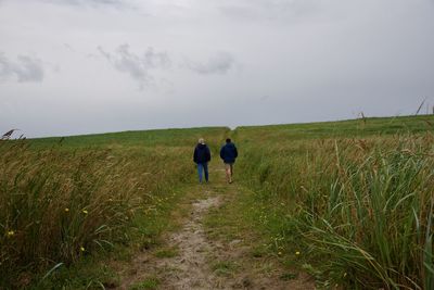 Rear view of men walking on field against sky