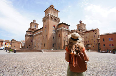 Rear view of traveler girl walking towards este castle of ferrara, italy.