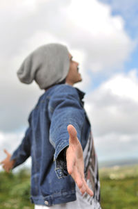 Side view of man with arms outstretched standing on field against sky