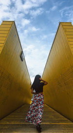 Rear view of woman standing by building against sky