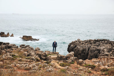 High angle view of man standing on rock by sea against clear sky