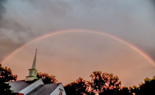 Low angle view of rainbow over trees against sky