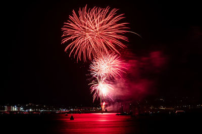 Firework display reflecting on river against sky at night