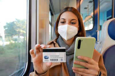 Woman with ffp2 kn95 protective mask traveling with train paying with her credit card on smart phone