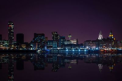 Illuminated city skyline by river against sky at night