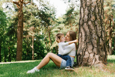 Young caucasian mother kisses her three-year-old son on the cheek while sitting in the park