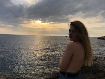 Woman standing at beach against sky during sunset