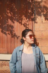 Young woman looking away while standing against wall