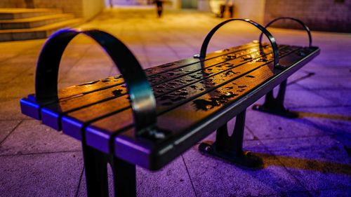 Close-up of wet metallic bench on sidewalk in city
