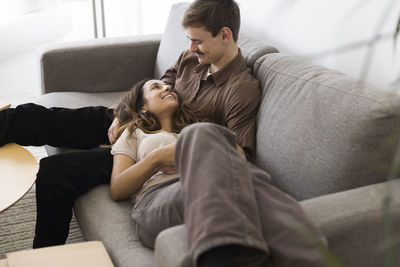 Smiling woman lying down on boyfriend's lap sitting on sofa at home