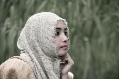 Close-up of thoughtful mid adult woman wearing hijab looking away while sitting against plants