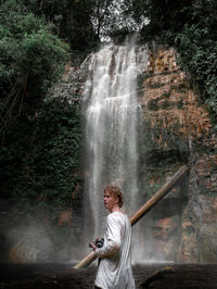 Full length of man standing against waterfall in forest