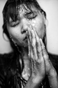 Close-up of young woman with hands clasped standing below shower