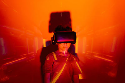 Little boy leaning on wall and exploring virtual reality under orange neon light