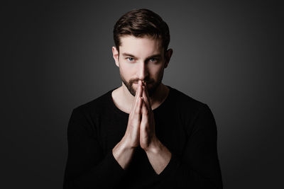 Portrait of young man standing against black background