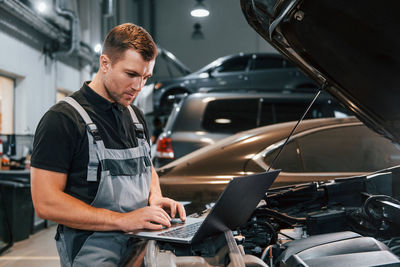 Using laptop. man in uniform is working in the auto service.