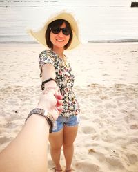 Portrait of woman holding man hand while wearing sunglasses on beach