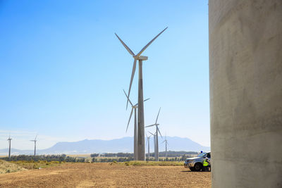 Windmills on field against clear blue sky