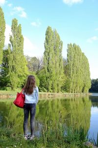 Rear view of woman standing with purse at lakeshore against trees