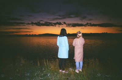 Rear view of couple standing by sea against sky during sunset