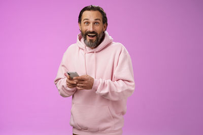 Portrait of man holding smart phone against pink background