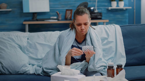 Sick woman holding medicine resting on sofa at home