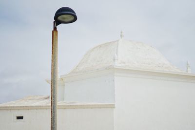 Low angle view of street light by building against sky