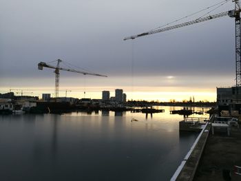 Silhouette cranes by river against sky during sunset