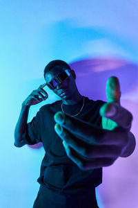 Concentrated young african american male millennial in casual clothes and vr glasses reaching out hand toward camera against colorful background
