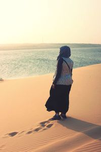 Rear view of woman walking on beach against clear sky
