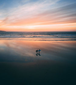 High angle view of people walking at beach against sky during sunset