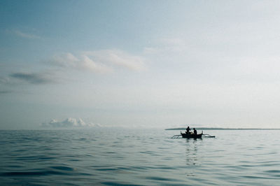 People on outrigger boat in sea against sky