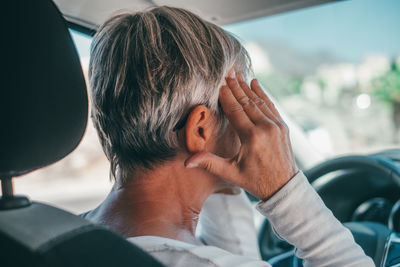 Close-up of senior woman with head in hands sitting in car