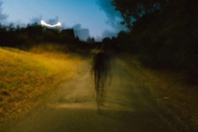 Blurred motion of person walking on road against sky at night