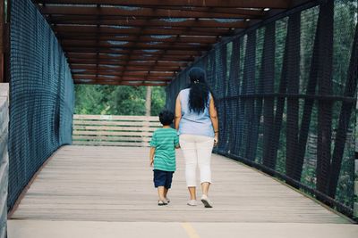 Rear view of mother and son walking on footbridge