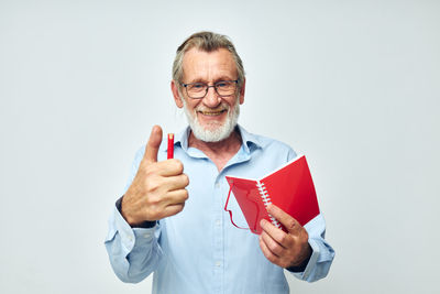 Portrait of smiling senior man holding book against white background