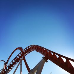 Low angle view of rollercoaster against clear blue sky