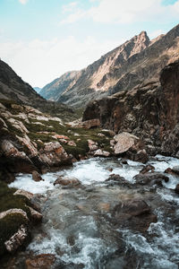 Scenic view of stream flowing through rocks against sky